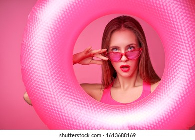 Summer vacation. Studio portrait of pretty young woman holding big pink rubber ring on pink background.