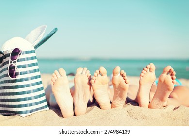 Sommerurlaub, Sonnenbaden und Pediküre - drei Frauen liegen am Strand mit Strohhut, Sonnenbrille und Tasche
