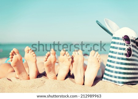 summer vacation, sunbathing and pedicure concept - three women lying on the beach with straw hat, sunglasses and bag
