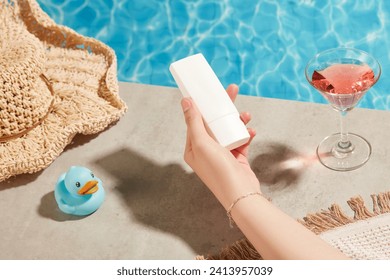 Summer vacation with swimming pool and clear blue water, decorated hats and wine glasses. The woman's hand is holding a tube of sunscreen with no label for the design. Sun protection concept - Powered by Shutterstock