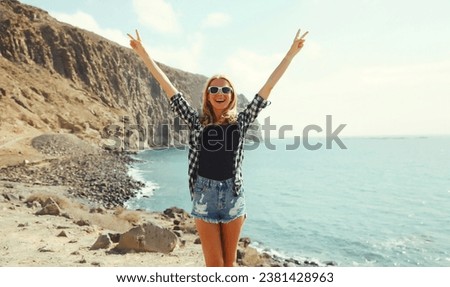 Summer vacation and travel, happy cheerful young woman raising her hands up on sea coast with mountain background, Tenerife, Canary Islands, Spain