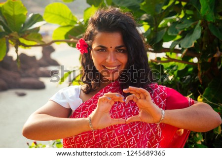 summer vacation Valentine's day in India girl sent air kiss and heart shape.beautiful woman wearing indian traditional outfit red wedding saree sari in tropical trees paradise island sea ocean beach