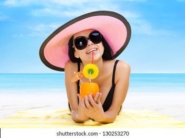 Summer Vacation Woman Lying On Beach Yellow Sand Towel Smile Drink Tropical Cocktail With Straw, Sun Tanned Body, Girl Wear Pink Hat, Sunglasses, Over Sea Blue Sky, Concept Holiday Travel