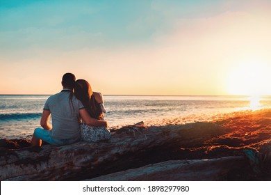 Summer vacation. A young couple posing against the sea, sitting on the rocks in an embrace. Rear view. Copy space. Sunset.