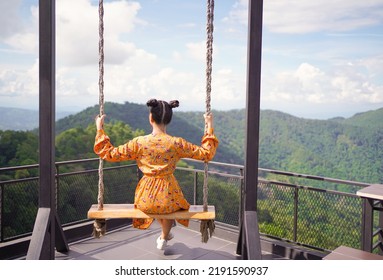Summer Vacation. A Young Woman Sits On A Tree Rope Swing On High