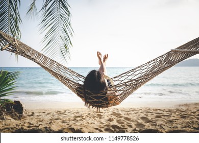 Summer vacations concept, Happy woman with white bikini, hat and shorts Jeans relaxing in hammock on tropical beach at sunset, Koh mak, Thailand