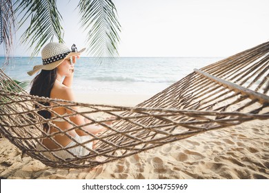 Summer vacations concept, Happy woman with white bikini, hat and shorts Jeans relaxing in hammock on tropical beach at sunset, Koh mak, Thailand - Shutterstock ID 1304755969