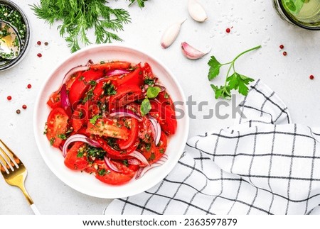 Summer vegan tomato salad with parsley, red onion, garlic, pepper and olive oil dressing, white table background, top view