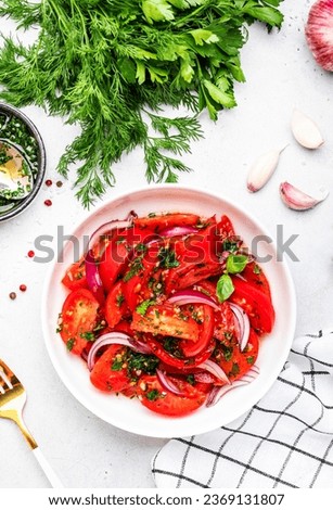 Summer vegan tomato salad with parsley, red onion, garlic, pepper and olive oil dressing, white table background, top view