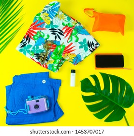 Summer vibes hawaii shirt outfit flat lay with accessories on yellow background (orange bag, phone, camera, sunglasses, sunscreen lotion)