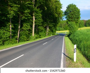 Summer View On Empty Automobile Road With Kilometer Post Among Green Fiels And Forest Trees. Empty Car Road. European Car Travel Concept