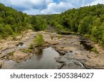 A summer view of the top of Little River Falls in Little River Canyon National Preserve, Alabama. Lush green foliage lines the river bed, and shallow pools of water form in the rock layers.