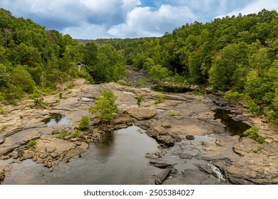 A summer view of the top of Little River Falls in Little River Canyon National Preserve, Alabama. Lush green foliage lines the river bed, and shallow pools of water form in the rock layers. - Powered by Shutterstock