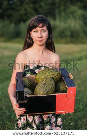 Summer, village. Young woman in dress holding box full of melons