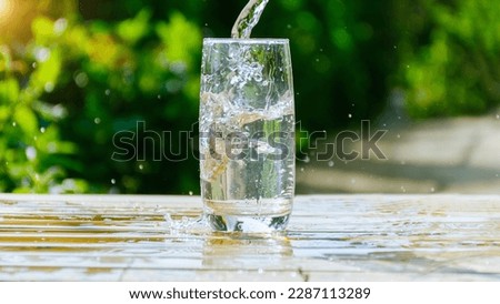 Summer water glass drink water pouring in to glass pure fresh water  freshness.Health water flows into a glass placed on a wooden bar natural green background