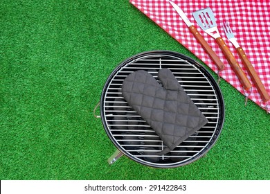 Summer Weekend Or Holiday BBQ Grill Party Or Picnic Concept. Park Or Backyard Fresh Lawn In The Background. Portable Kettle Charcoal Grill And Tools Close-up