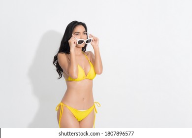 Summer woman portrait. Asian woman wearing a yellow bikini dress in a standing fashion, with a white sunglasses, in a summer fashion at studio shot on isolated white background.