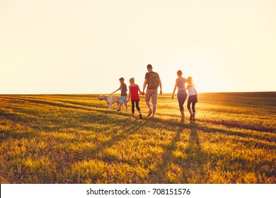 Summertime In The Countryside. Silhouettes Of The Family With Dog On The Trip At The Sunset.