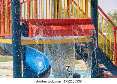 Summertime Fun For The Kids At The Splash Pad To Play With Water Falling From Bright Colored Red Fountain To Pool Below.