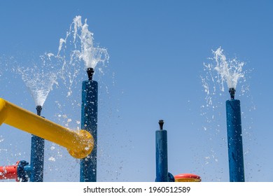 Summertime Fun For The Kids At The Splash Pad To Play With Water Falling From Bright Colored Fountains To Blue Sky.