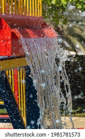 Summertime Fun For The Kids At The Splash Pad To Play With Water Falling From Bright Colored Red Fountain To Pool Below (portrait View).