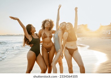 Summertime. Group of happy diverse female friends laughing while dancing in swimwear on the beach at sunset, women enjoying their summer vacation - Powered by Shutterstock