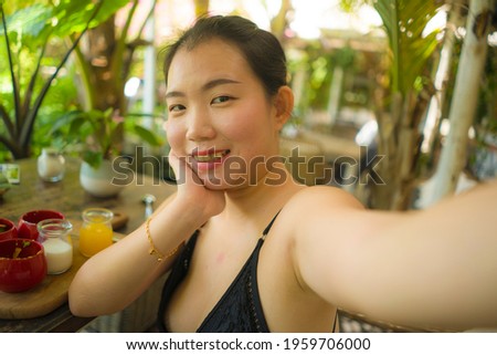 summertime lifestyle portrait of young attractive and happy Asian Korean woman taking selfiei having healthy lunch with organic food and orange juice during holidays 