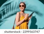summertime pleasure asia female woman in summer yellow dress wear sun glasses hand using smartphone text conversation with cheerful enjoy summer vacation trip studio shot on colour background 