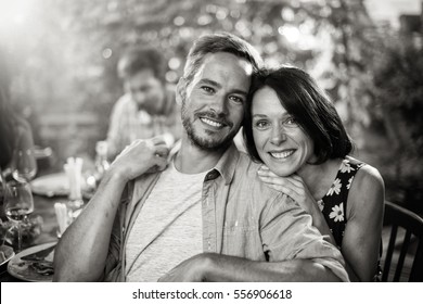 Summertime, portrait of a beautiful couple looking at the camera, they are sitting with friends around a terrace table to share good times. Black and white - Powered by Shutterstock