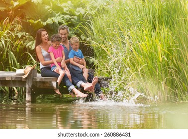 summertime, portrait of an happy family sitting on the edge of a wooden pontoon, feet in the river and making splashes - Shutterstock ID 260886431