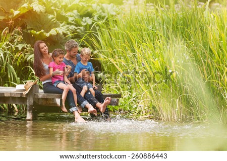 summertime, portrait of an happy family sitting on the edge of a wooden pontoon, feet in the river and making splashes