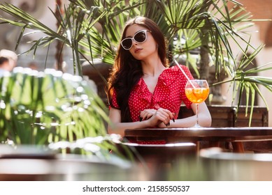 Summertime Portrait Of Relaxed Young Woman In Sunglasses Straw Hat With Aperol Spritz Drink Sitting On Summer Terrace