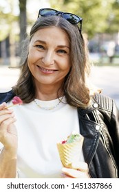 Summertime Shot Of Cefree Happy Female In Her Sixties Enjoying Sunny Summer Morning In City Park, Walking Alone And Eating Strawberry Ice Cream In Waffle Cone, Using Wooden Stick And Smiling