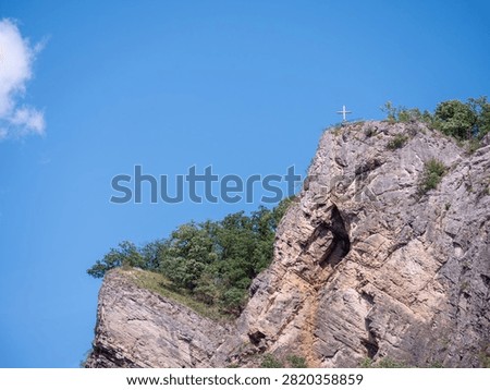 Summit cross above the dramatic limestone cliffs of Svatý Jan pod Skalou, with the Pod křížem Cave hidden beneath the rock, in the Bohemian Karst, Czech Republic.