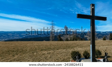 Summit cross on alpine meadow in West Styrian highland in Voitsberg, Styria, Austria. Hiking in remote landscape of soft hills and forest in spring. Scenic view of idyllic mountains of Lavanttal Alps