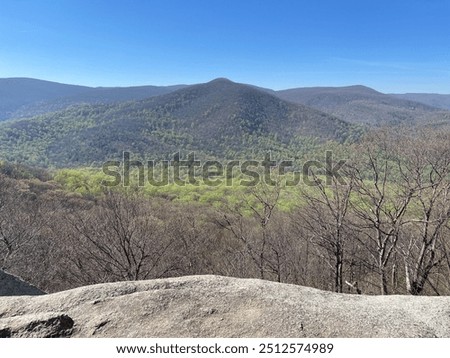 From the summit of Old Rag Mountain, the view unfolds to a lush green valley below, with vibrant forests and rolling hills stretching endlessly, offering a breathtaking glimpse of Shenandoah.