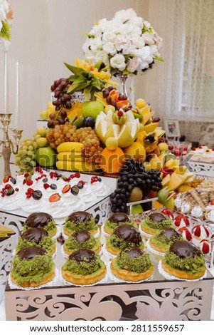 Sumptuous festive table laden with elegant chocolate cakes, sweet berry meringues, and a towering pyramid of vibrant fresh fruit