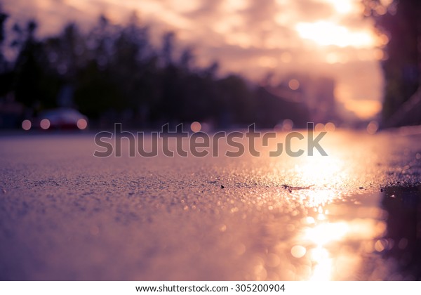Sun after the rain in the city, view of the cars\
with a level of puddles on the pavement. Image in the soft\
orange-purple toning