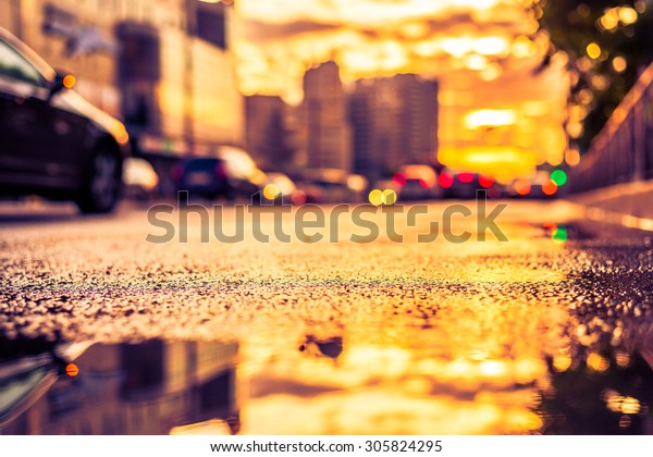 Sun after the rain in the city, view of the cars\
with a level of puddles on the pavement. Image in the yellow-purple\
toning