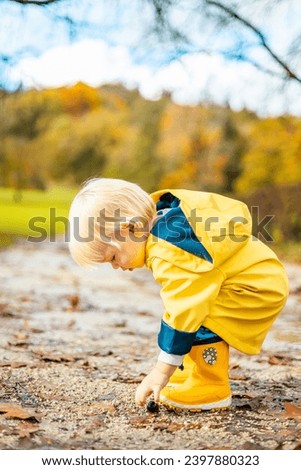 Image, Stock Photo Sun always shines after the rain. Small bond infant boy wearing yellow rubber boots and yellow waterproof raincoat walking in puddles in city park on sunny rainy day.