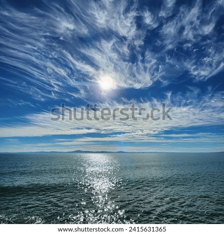 the sun among scattering cirrus clouds over the choppy sea. path of sun glare on the sea surface