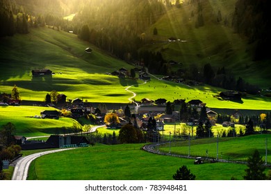 Sun beams lighting through the clouds and falling down to the little village on the hill, vivid colors of sunset, waves of green fields, Chateau-dOex, Switzerland