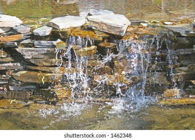 The sun beating down on a small man made waterfall in the park.