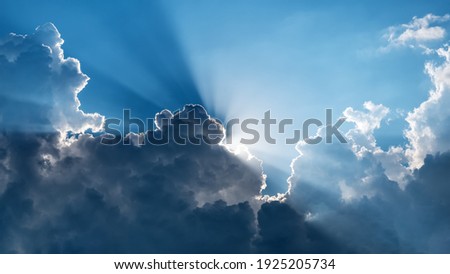 Sun behind dark clouds with sun rays on blue sky background