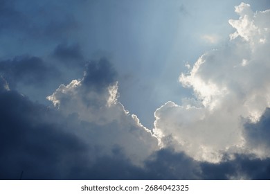 Sun behind dramatic clouds in a blue sky, creating a silver lining effect with beautiful light rays.