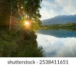 The sun behind the trees, shining through the leaves, illuminates the lake