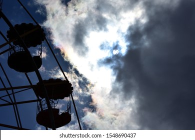 sun between clouds with polarized light and the silhouette of a ferris wheel