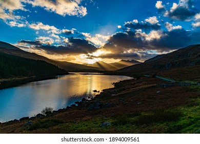 Sun Breaking Through Clouds Over Welsh Lake And Mountain