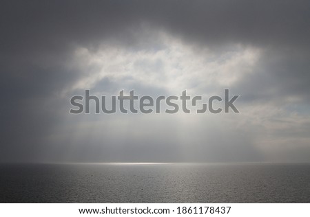 Sun breaks through the clouds above a misty, calm sea