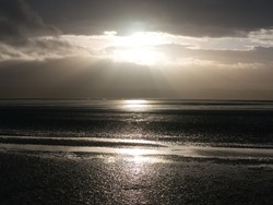 The Sun Breaks Through Clouds Over The Mudflats Of The Dee Estuary At Low Tide At West Kirby On Wirral In North West England. The Coast Of North West Wales Appears In The Distance. Taken In Winter.